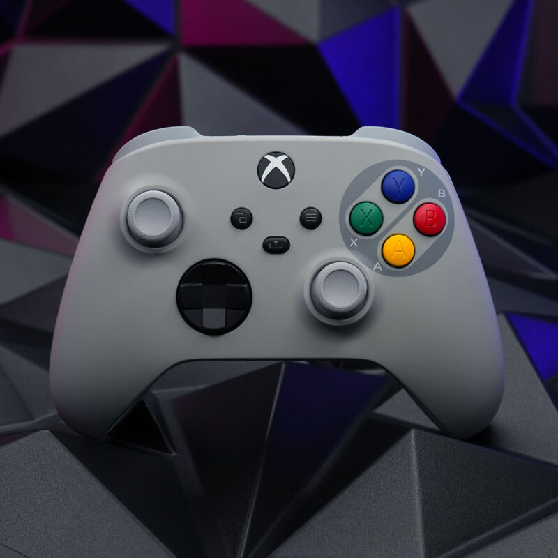 Custom SNES-themed Xbox Series X|S controller angled slightly, featuring a gray shell and colorful Super Famicom-style buttons, set against a dark geometric background.